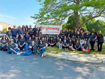 Group of Brightway staff in their gray and orange Brightway shirts posing in front of the Brightway sign.