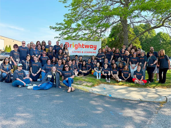 Group of Brightway staff in their gray and orange Brightway shirts posing in front of the Brightway sign.