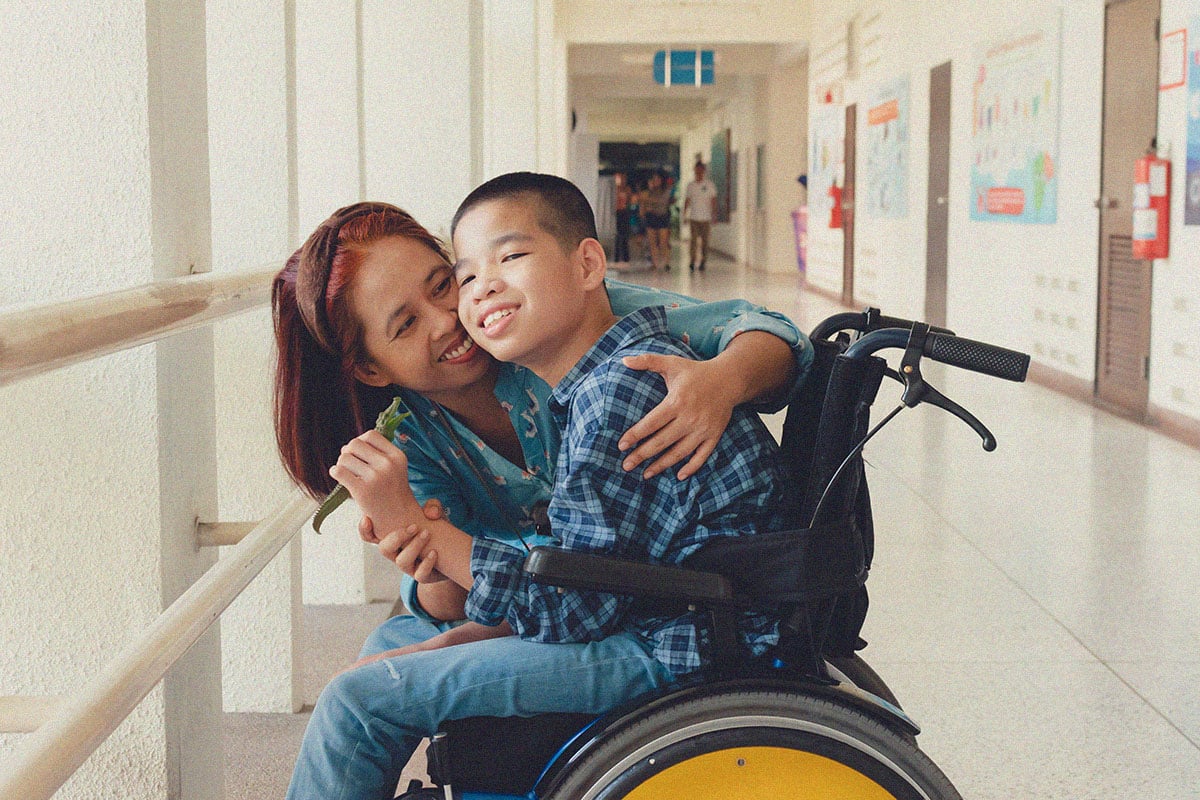 Mother and special child on wheelchair is smiling happily on background in school corridor