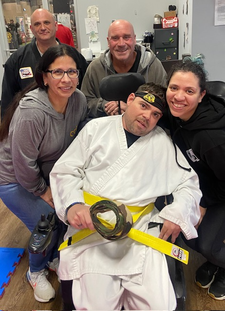 A man in mixed martial arts uniform with camo belt in hand surrounded by his Direct Support Team