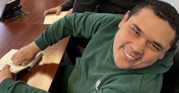 Young man in green sweatshirt smiling with a book