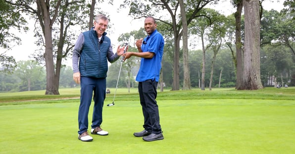 two men standing on the greens holding a putter