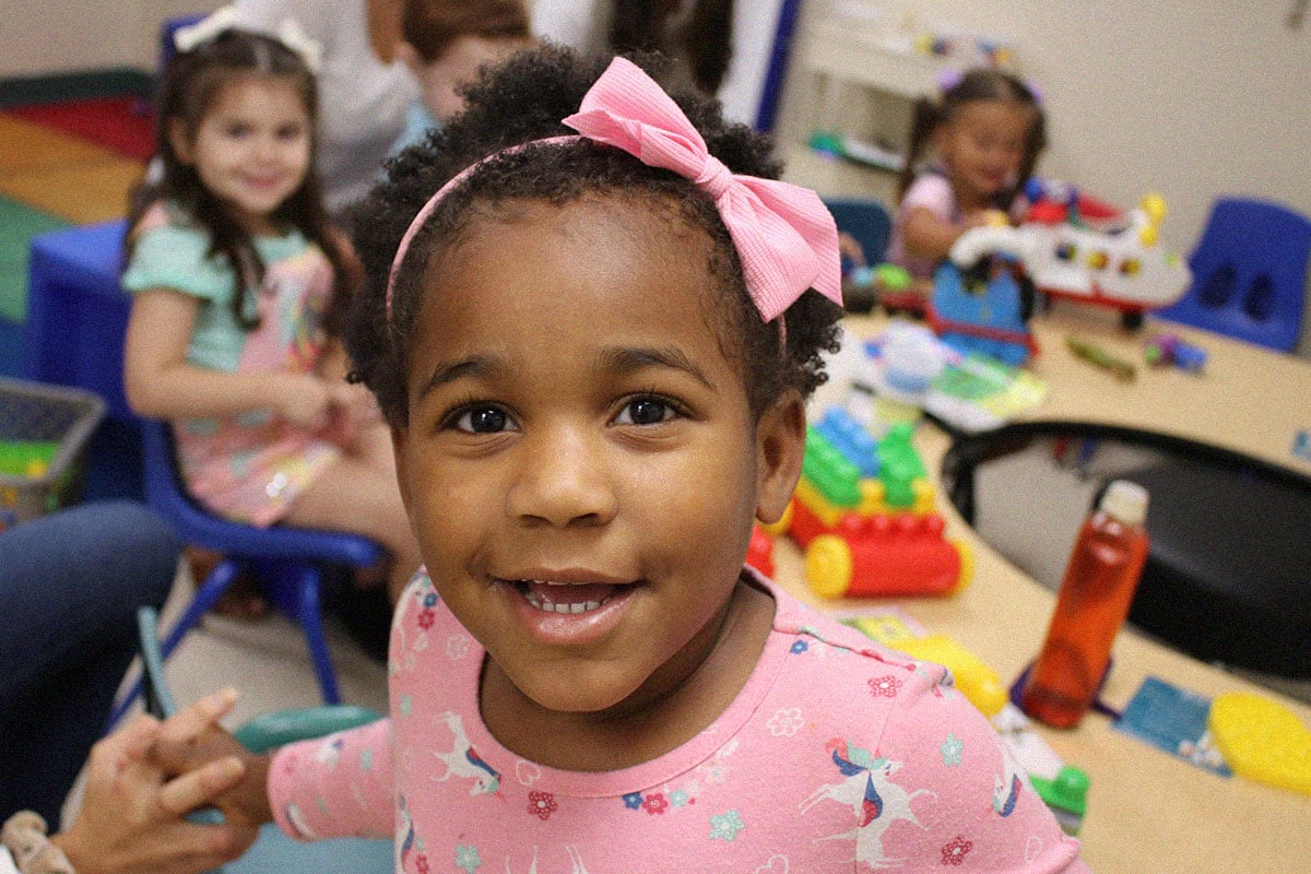 little girl smiling in classroom with other kids