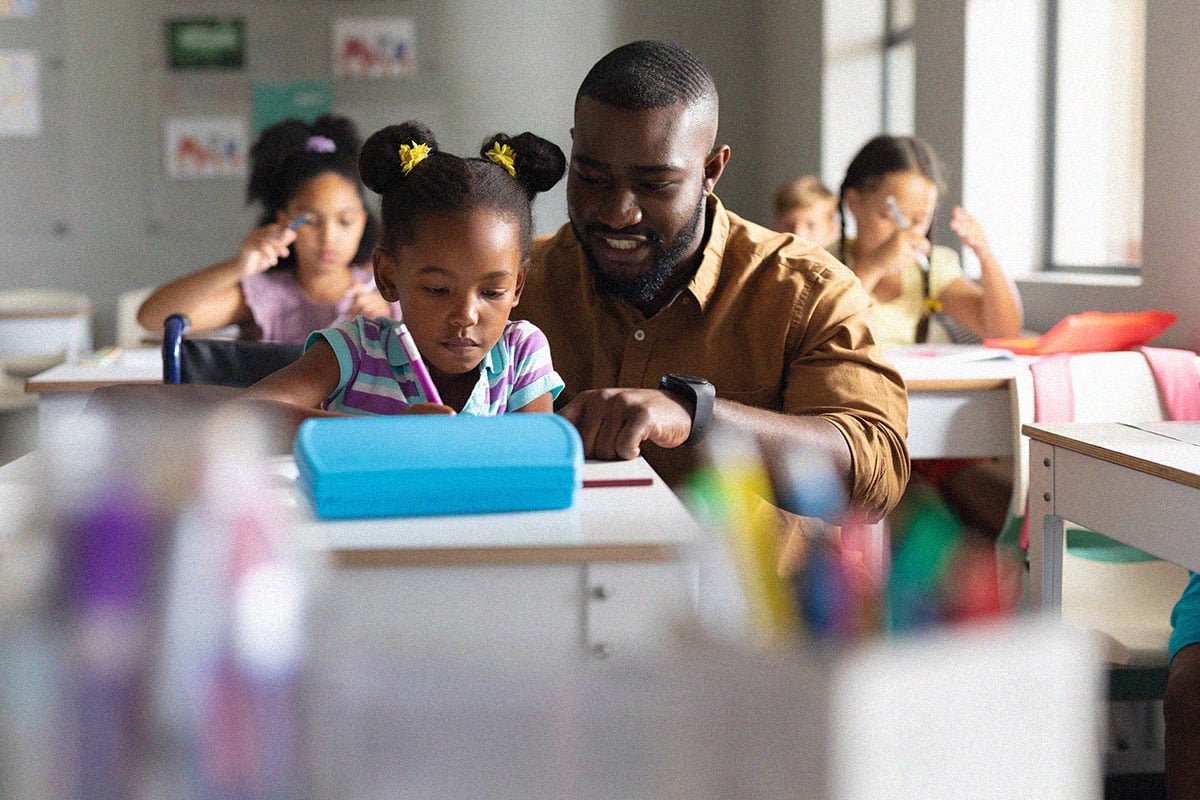 male-teacher-teaching-elementary-girl-on-wheelchair-in-class