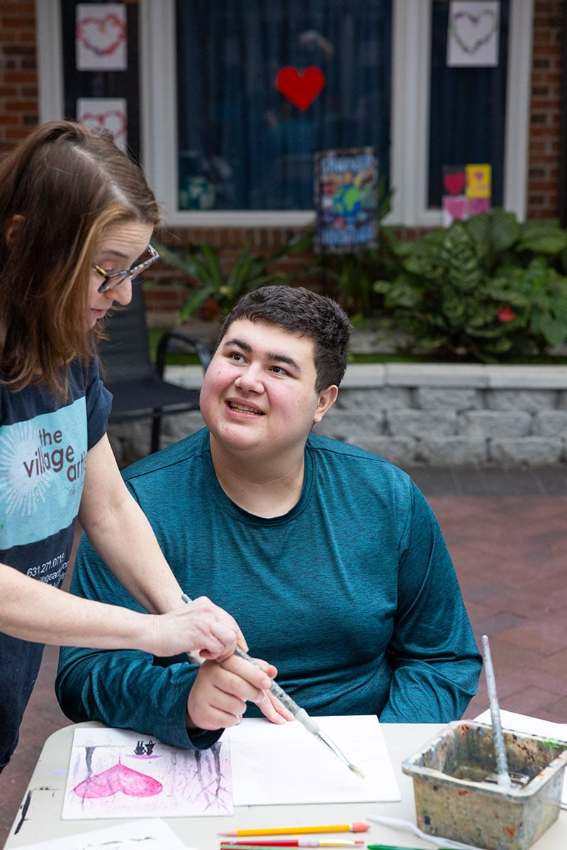 teacher helping male student paint outside