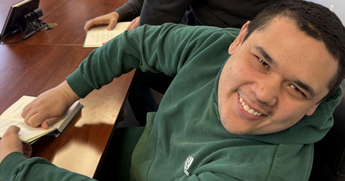 Young man in green sweatshirt smiling with a book